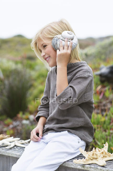 Primo piano di bambina che ascolta conchiglia in natura — Foto stock