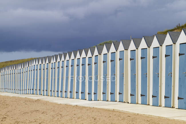 Francia, Francia Occidental, Saint-Gilles-Croix-de-Vie, cabañas de baño bajo nubes tormentosas. - foto de stock