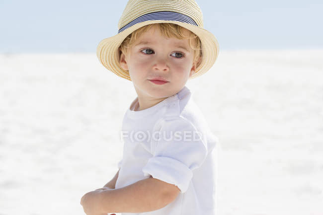 Крупный план милого мальчика в соломенной шляпе, играющего на пляже — стоковое фото