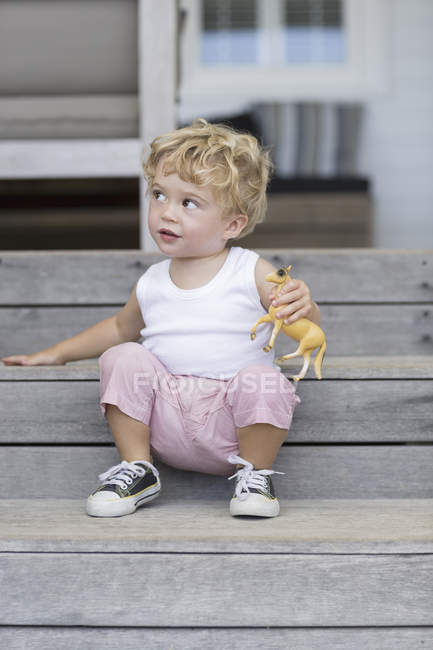 Cute baby boy sitting on steps with toy — Stock Photo