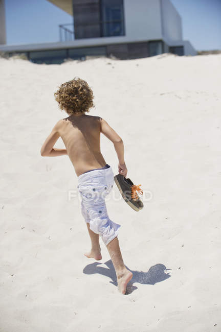 Menino sem camisa correndo na praia ensolarada — Fotografia de Stock