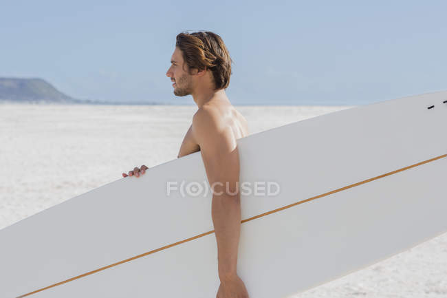 Young man carrying surfboard on beach — Stock Photo