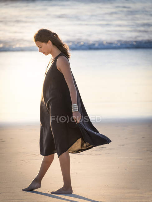 Jeune femme rêveuse en robe marchant sur la plage — Photo de stock