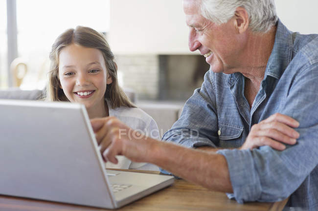 Hombre mostrando portátil a la nieta y sonriendo - foto de stock
