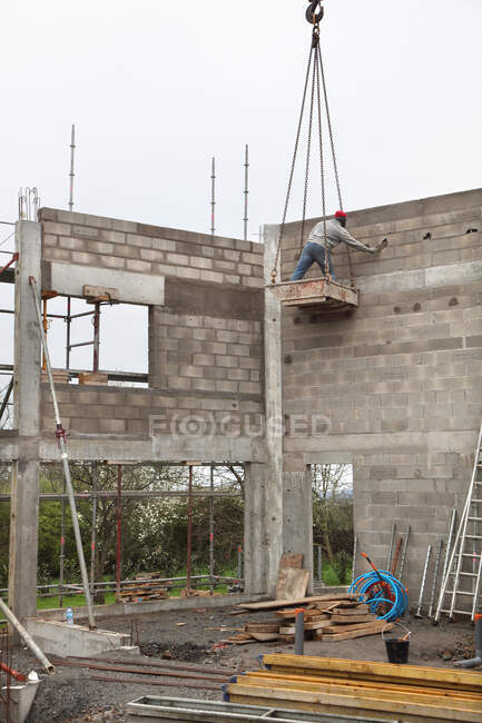 Francia, edificio de la casa, levantando las paredes de la casa. Problema de seguridad con el manejo por el equipo de construcción. Brecha de seguridad: albañil en el cubo sin casco - foto de stock