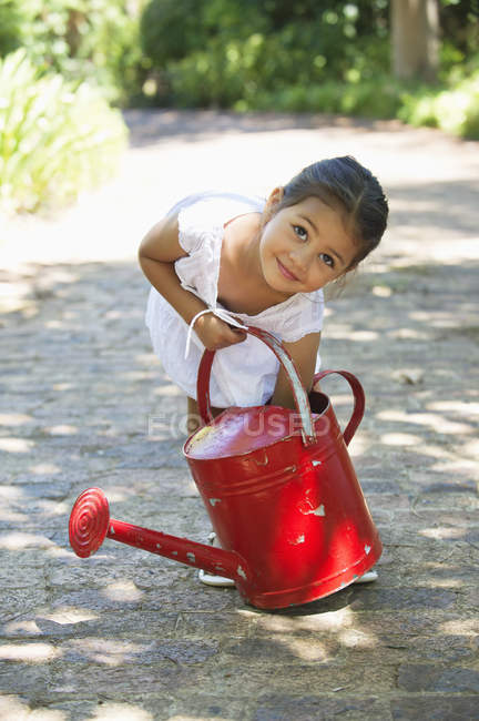 Cute little girl picking up watering can on path in countryside — Stock Photo