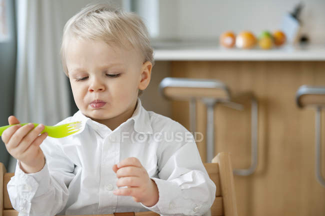 Kleiner Junge isst mit Gabel und macht Gesicht in Küche — Stockfoto