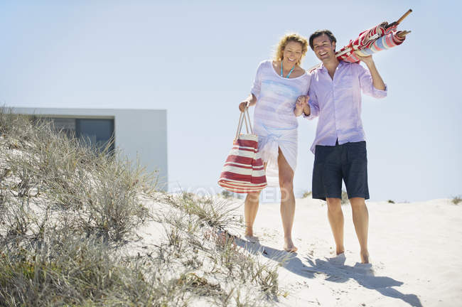 Casal feliz andando na praia com saco e guarda-chuva de praia — Fotografia de Stock