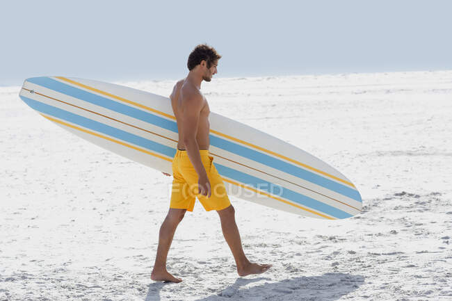Бічний профіль чоловіка, що носить дошку для серфінгу на пляжі — стокове фото