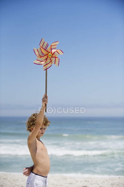 Junge mit Windrad am Strand unter blauem Himmel — Stockfoto