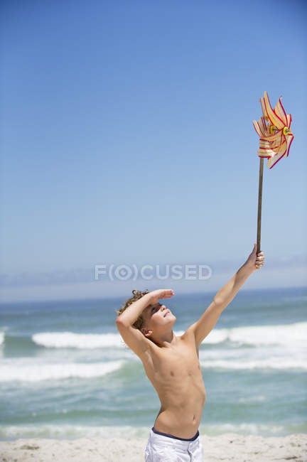 Menino segurando pinwheel na praia sob o céu azul — Fotografia de Stock