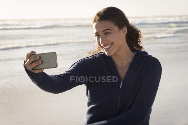 Jeune femme prenant selfie avec smartphone sur la plage — Photo de stock