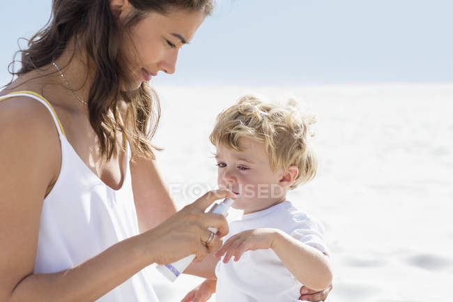 Frau sprüht Sonnencreme auf Babyhand am Strand — Stockfoto