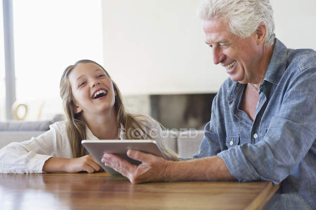 Девушка смеется, когда дедушка использует цифровой планшет за столом — стоковое фото