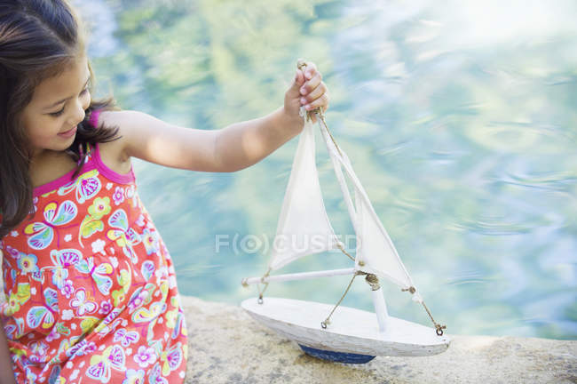 Little girl sitting at swimming pool and with boat toy — Stock Photo
