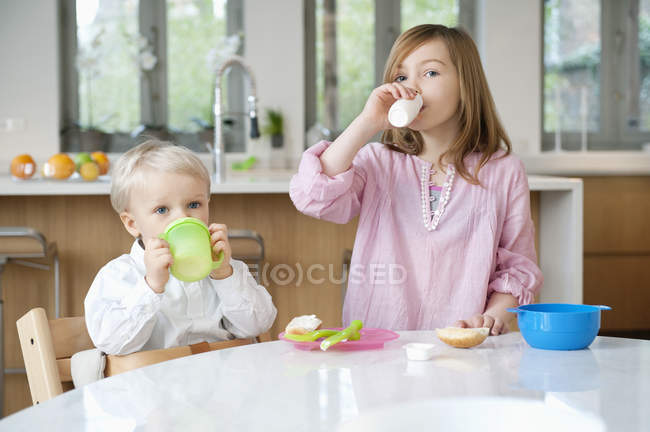 Портрет усміхненої дівчини, яка посміхається пити молоко з братом на кухні — стокове фото