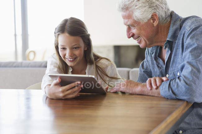 Girl using digital tablet with grandfather sitting at desk — Stock Photo