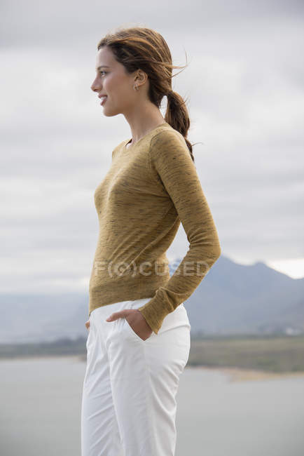 Confident young woman standing at lake shore and looking at view — Stock Photo