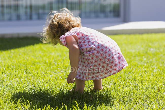 Вид сзади на симпатичную девочку в платье, стоящую на зеленой лужайке — стоковое фото