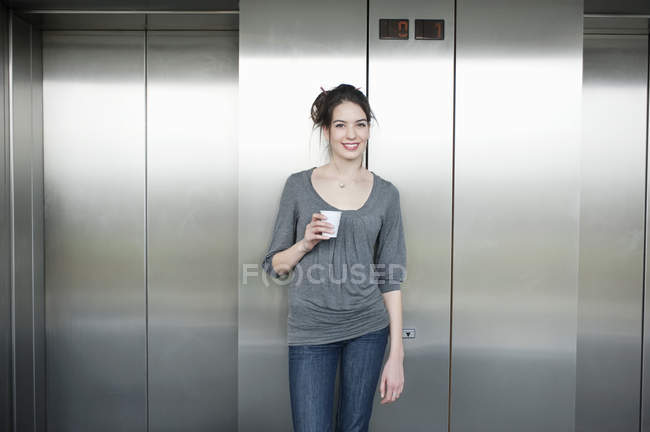 Businesswoman holding disposable cup and smiling in front of elevator — Stock Photo