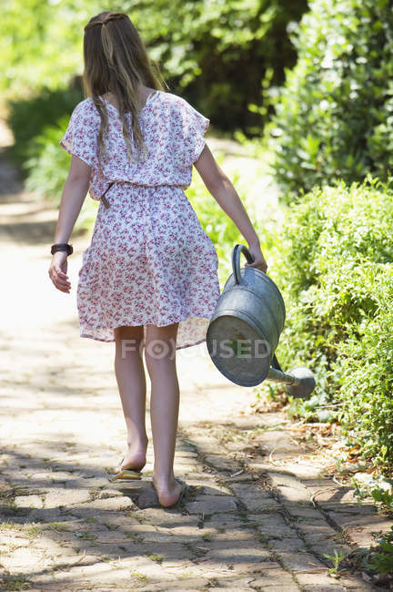 Rear view of little girl walking on path in garden with watering can — Stock Photo