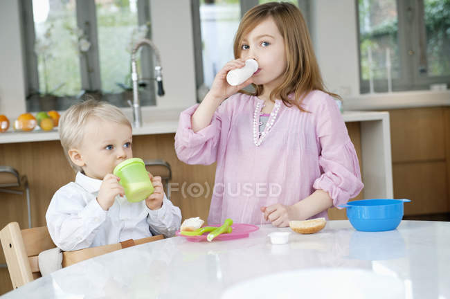 Портрет усміхненої дівчини, яка посміхається пити молоко з братом на кухні — стокове фото