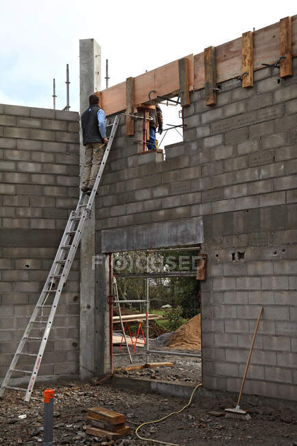 Francia, edificio de la casa. Levantamiento de las paredes de la casa. Seguridad en un andamio / escala. Instalación de un encofrado de hormigón - foto de stock