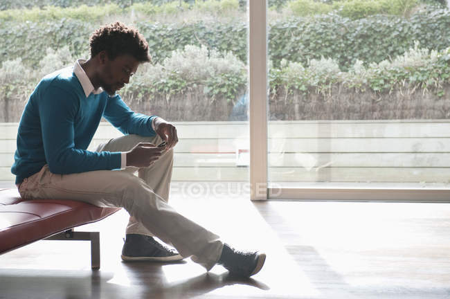 Man text messaging with mobile phone on bench in room — Stock Photo