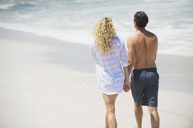 Вид сзади на пару, идущую по пляжу, держась за руки — стоковое фото