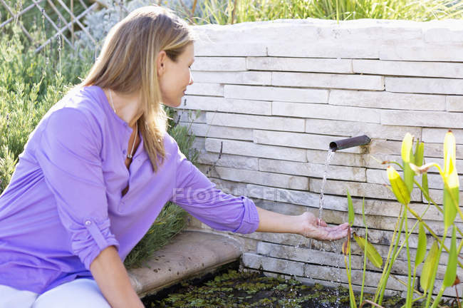 Jovem mulher com a mão sob água corrente no jardim — Fotografia de Stock