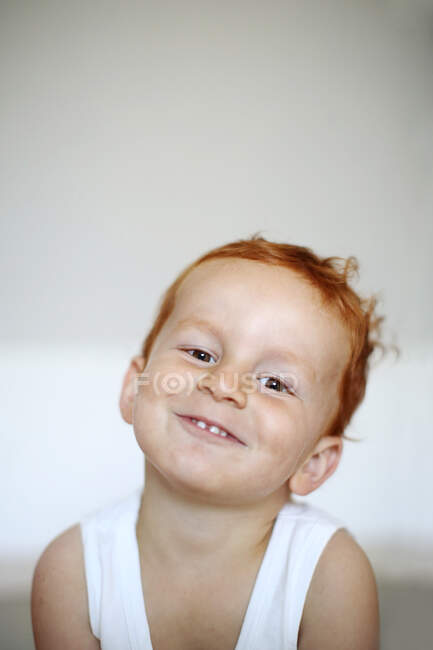 Portrait of a red-haired little boy wearing a tank top smilling, indoors — Stock Photo