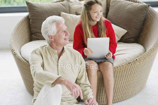 Старший чоловік сидить з онукою тримає цифровий планшет на дивані — стокове фото