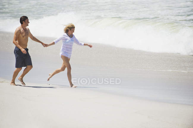 Пара бегущих по песчаному пляжу держащихся за руки — стоковое фото