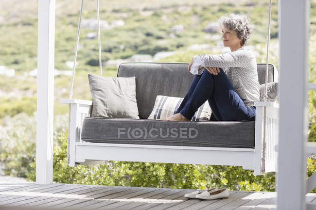 Felice donna matura seduta sull'altalena in veranda — Foto stock