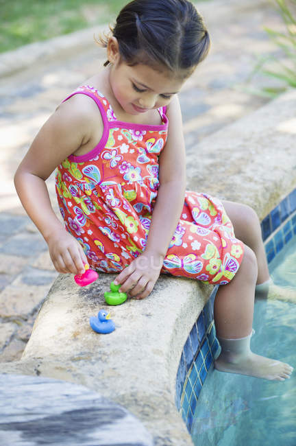 Little girl playing with rubber ducks at edge of swimming pool — Stock Photo