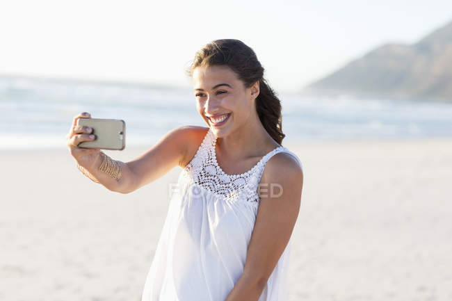 Jeune femme heureuse prenant selfie avec smartphone sur la plage — Photo de stock