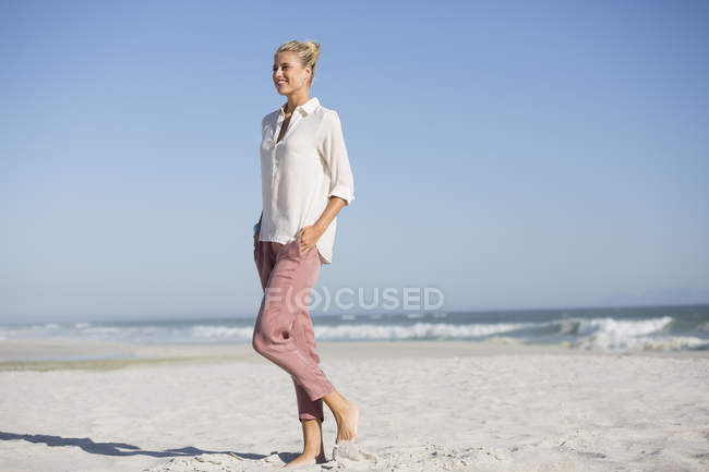 Высокая улыбающаяся молодая женщина, идущая по солнечному пляжу — стоковое фото