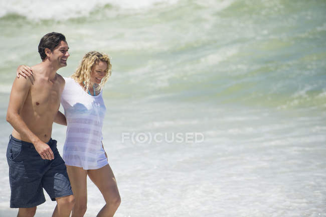Улыбающаяся обнимающая пара, идущая по пляжу — стоковое фото
