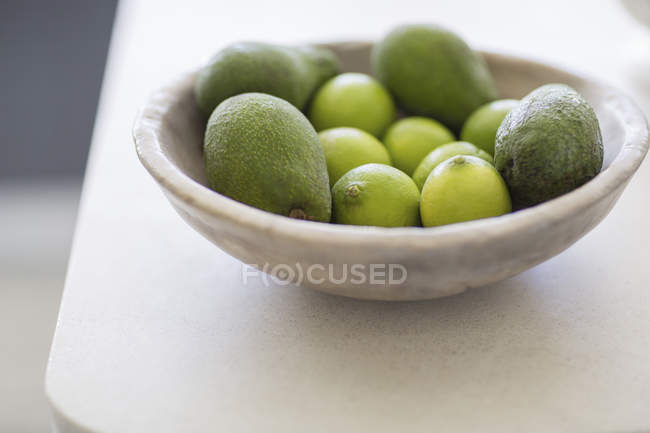 Close-up de limões e abacates em tigela na mesa branca — Fotografia de Stock