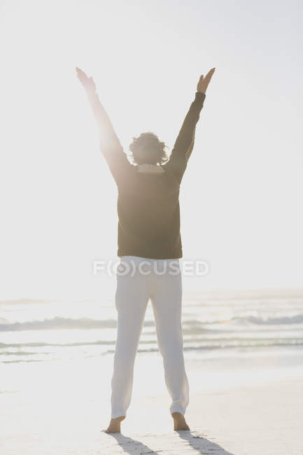 Вид ззаду жінки, що стоїть на пляжі з піднятими руками — стокове фото