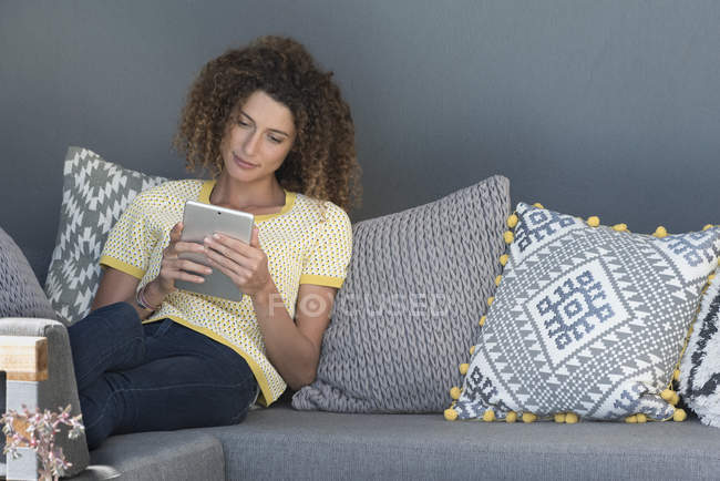 Женщина сидит на диване дома и с помощью цифрового планшета — стоковое фото