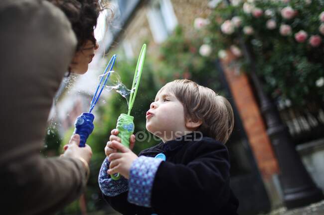 Piccolo ragazzo e sua madre soffiando bolle in strada — Foto stock