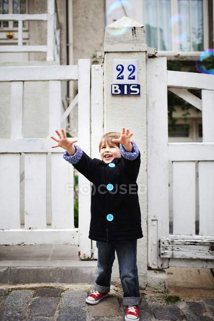 Niño con los brazos extendidos tratando de atrapar burbujas en la calle - foto de stock
