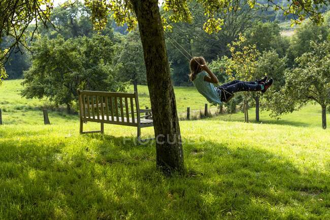 Francia, Normandía, niña disfrutando de un ir en un columpio en un hermoso jardín rural - foto de stock