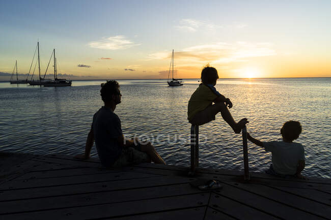 Un padre y sus dos hijos mirando al atardecer, Saint-Pierre, Martinica, Francia - foto de stock