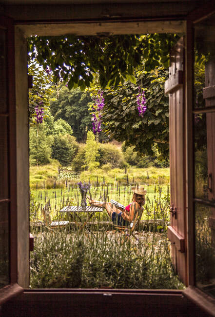 Mujeres jóvenes leyendo en el jardín visto por la ventana - foto de stock