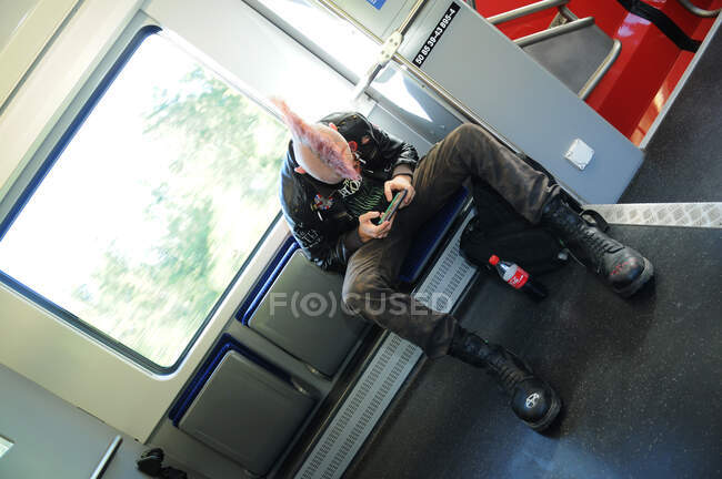 Schweiz: Punk mit pinkfarbenen Haaren starrt im Zug zwischen Genf und Lausanne auf sein Smartphone — Stockfoto