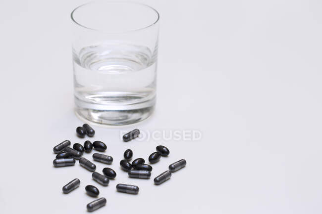 Close up of a box of activated charcoal capsules with a glass of water. — Stock Photo