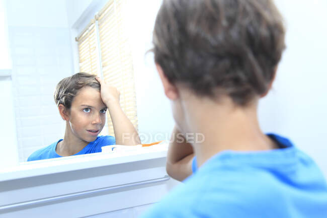 France, jeune garçon dans la salle de bain regardant les cheveux dans le miroir. — Photo de stock