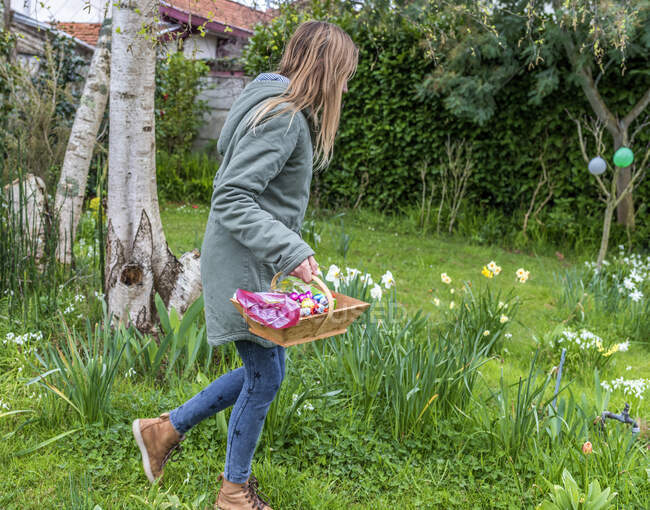 Francia, Pascua, adolescente cazando huevos de chocolate en un jardín. - foto de stock